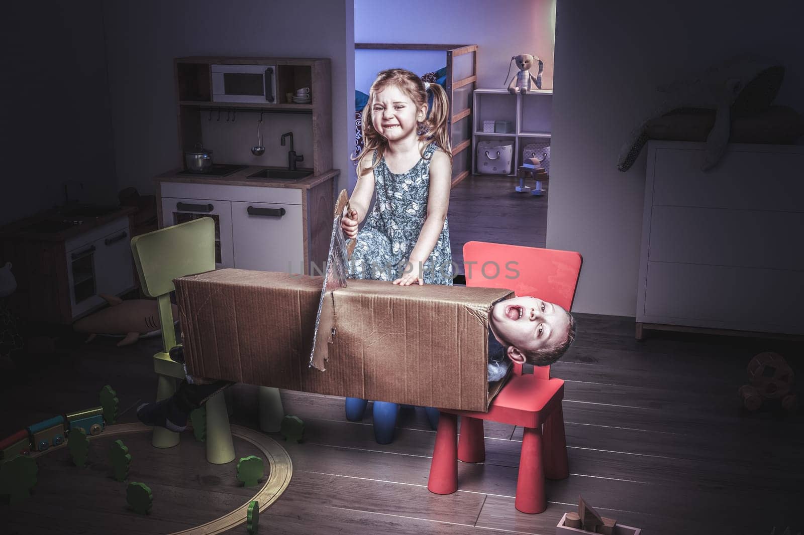 little 3 year old girl plays the magician and tries to cut her brother in two with a saw. Funny image, concept of carefree and childhood.
