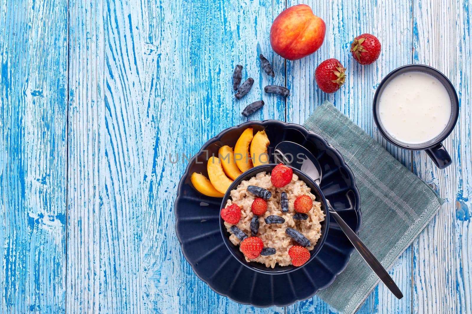 Mug with yogurt and oatmeal porridge with fresh berries and fruit in dark blue bowl on blue wooden background. Top view with copy space. Concept of healthy lifestyle, healthy food, dieting