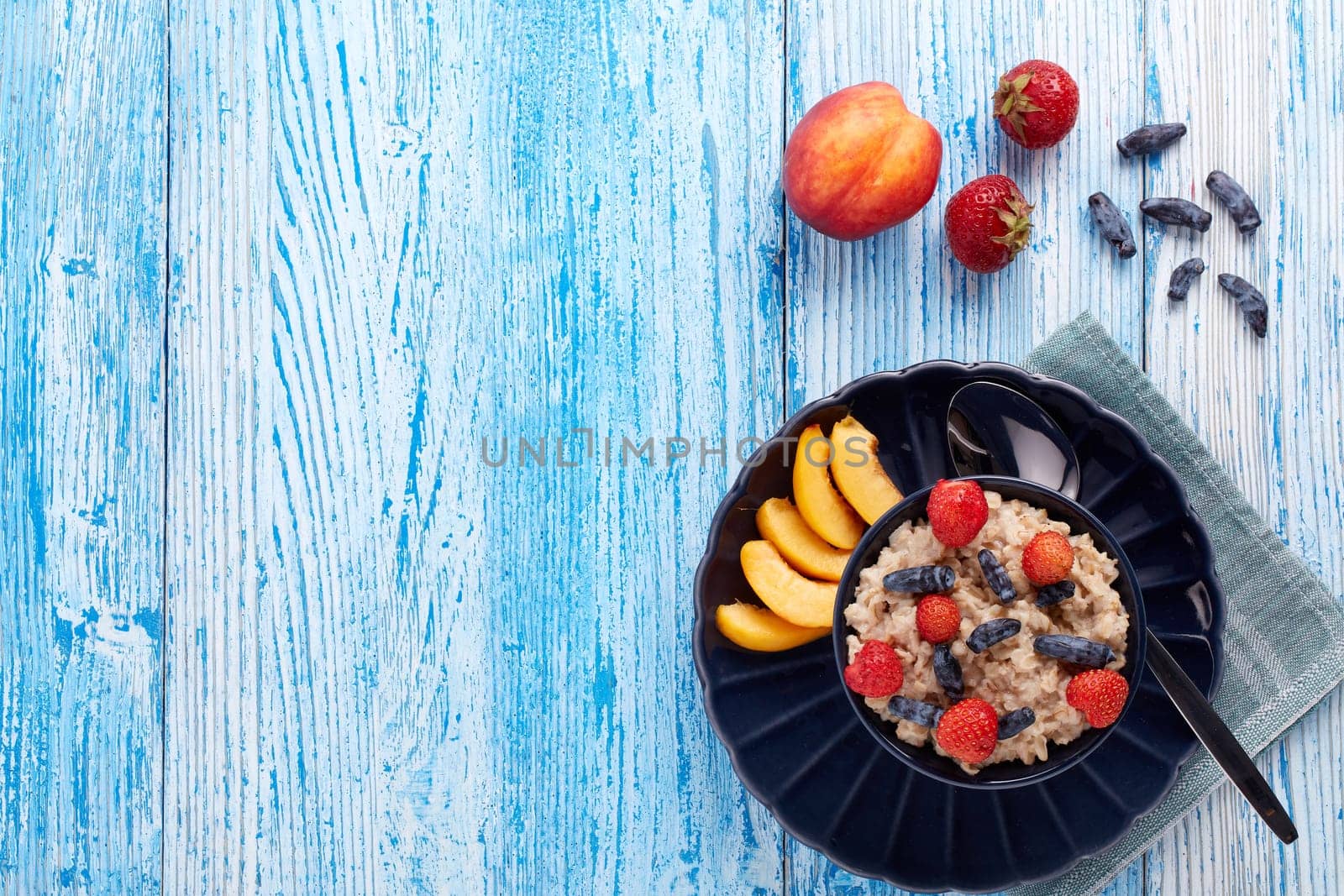 Oatmeal porridge with fresh berries and fruit in dark blue bowl on blue wooden background. Top view with copy space. Concept of healthy lifestyle, healthy food, dieting, vegetarian food