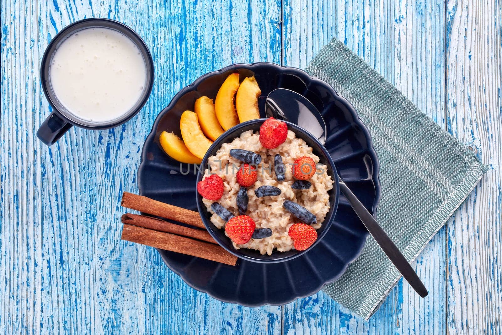 Mug with yogurt and oatmeal porridge with fresh berries and fruit in dark blue bowl on blue wooden background. Top view. Concept of healthy lifestyle, healthy food, dieting