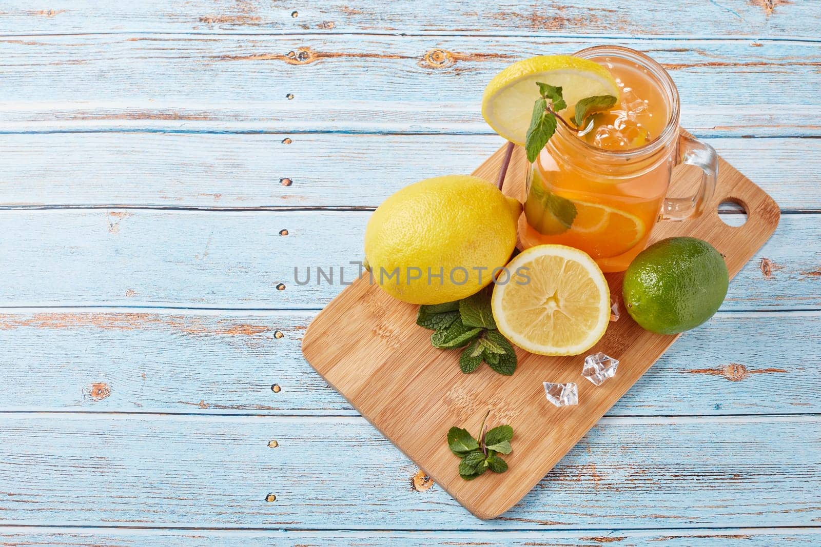 Citrus lemonade with ice, leaves of mint, lemon and lime slices standing on blue wooden table. Homemade lemonade with citruses. Healthy cool beverage