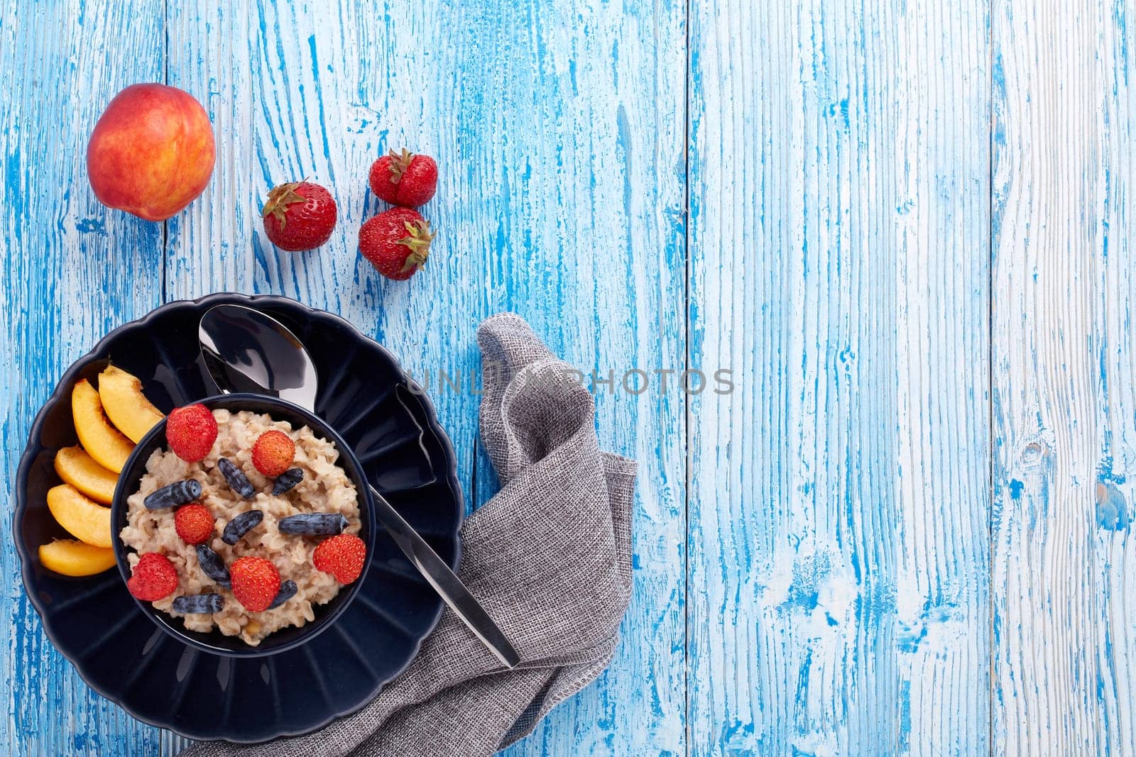 Oatmeal porridge with fresh berries and fruit in dark blue bowl on blue wooden background. Top view with copy space. Concept of healthy lifestyle, healthy food, dieting, vegetarian food