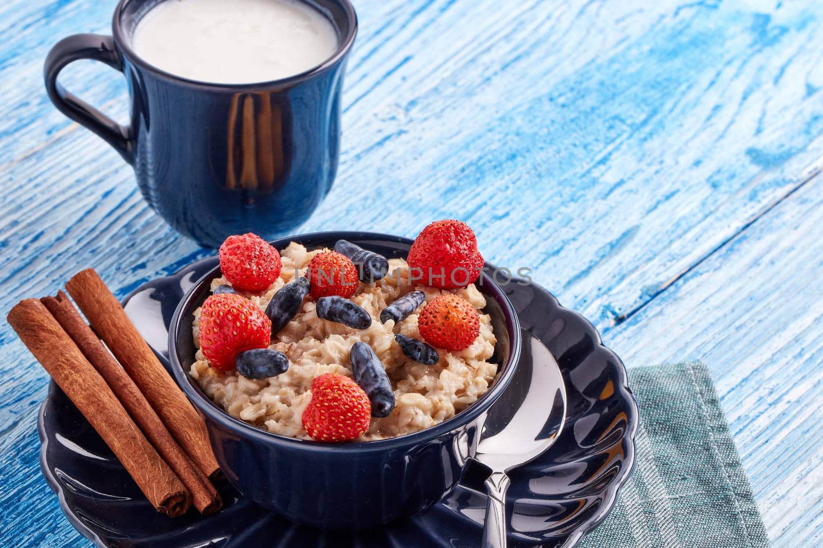 Mug with yogurt and oatmeal porridge with fresh berries and fruit in dark blue bowl on blue wooden background. Concept of healthy lifestyle, healthy food, dieting