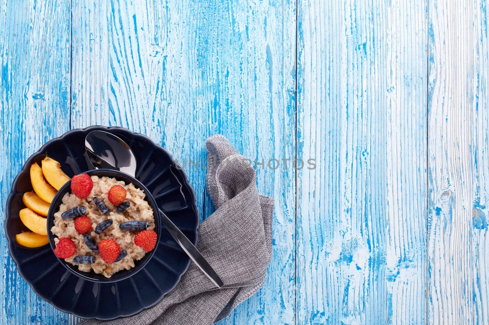 Oatmeal porridge with fresh berries and fruit in dark blue bowl on blue wooden background. Top view with copy space. Concept of healthy lifestyle, healthy food, dieting, vegetarian food