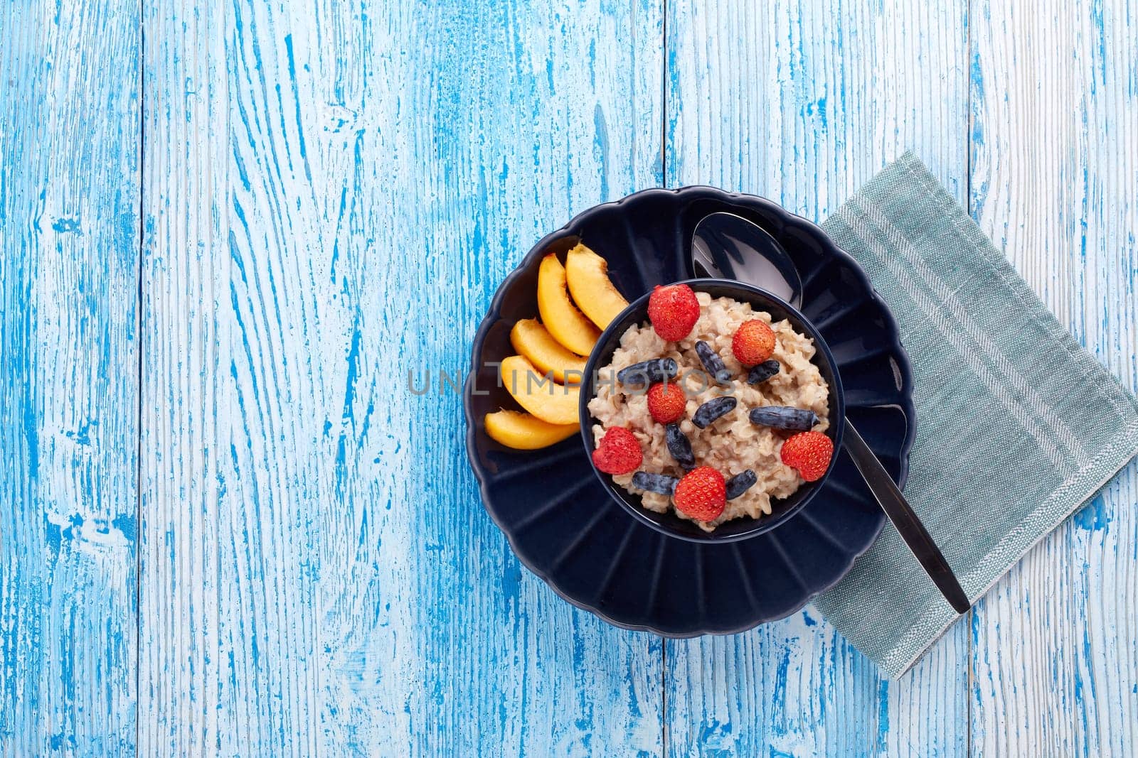 Oatmeal porridge with fresh berries and fruit in dark blue bowl on blue wooden background. Top view with copy space. Concept of healthy lifestyle, healthy food, dieting, vegetarian food