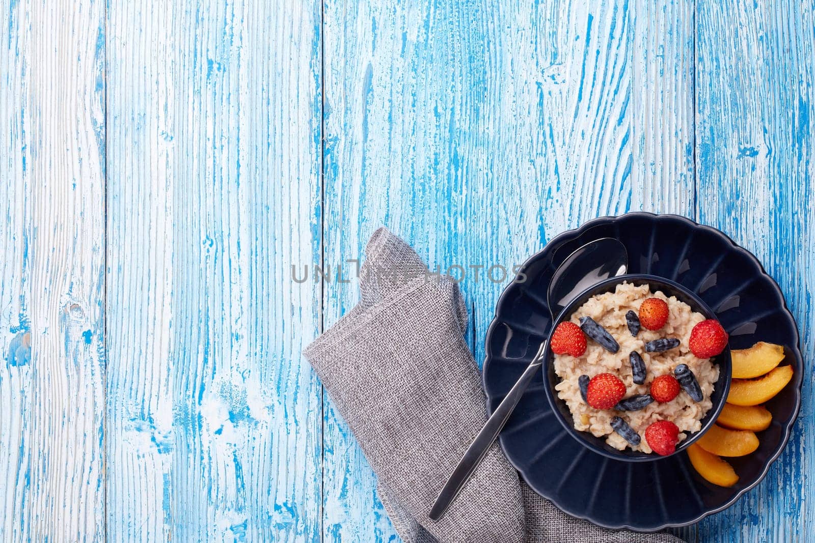 Oatmeal porridge with fresh berries and fruit in dark blue bowl on blue wooden background. Top view with copy space. Concept of healthy lifestyle, healthy food, dieting, vegetarian food