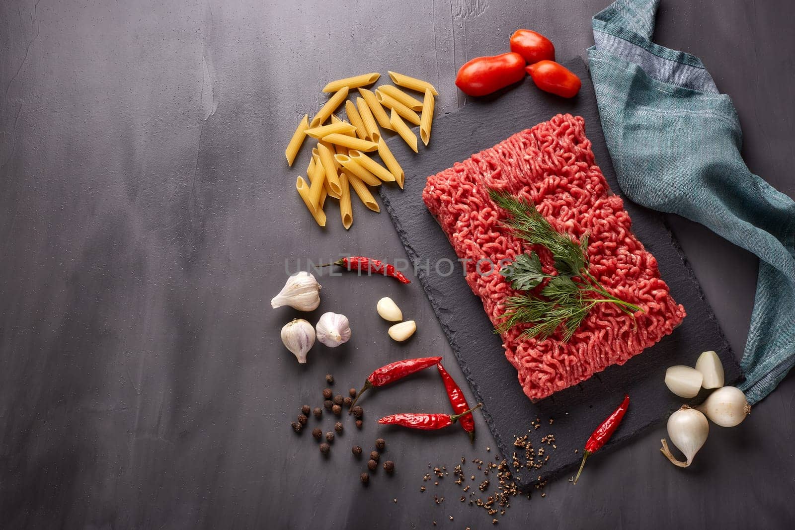 Still life with fresh forcemeat from beef, vegetables, pasta and spices on a dark background. Top view with copy space
