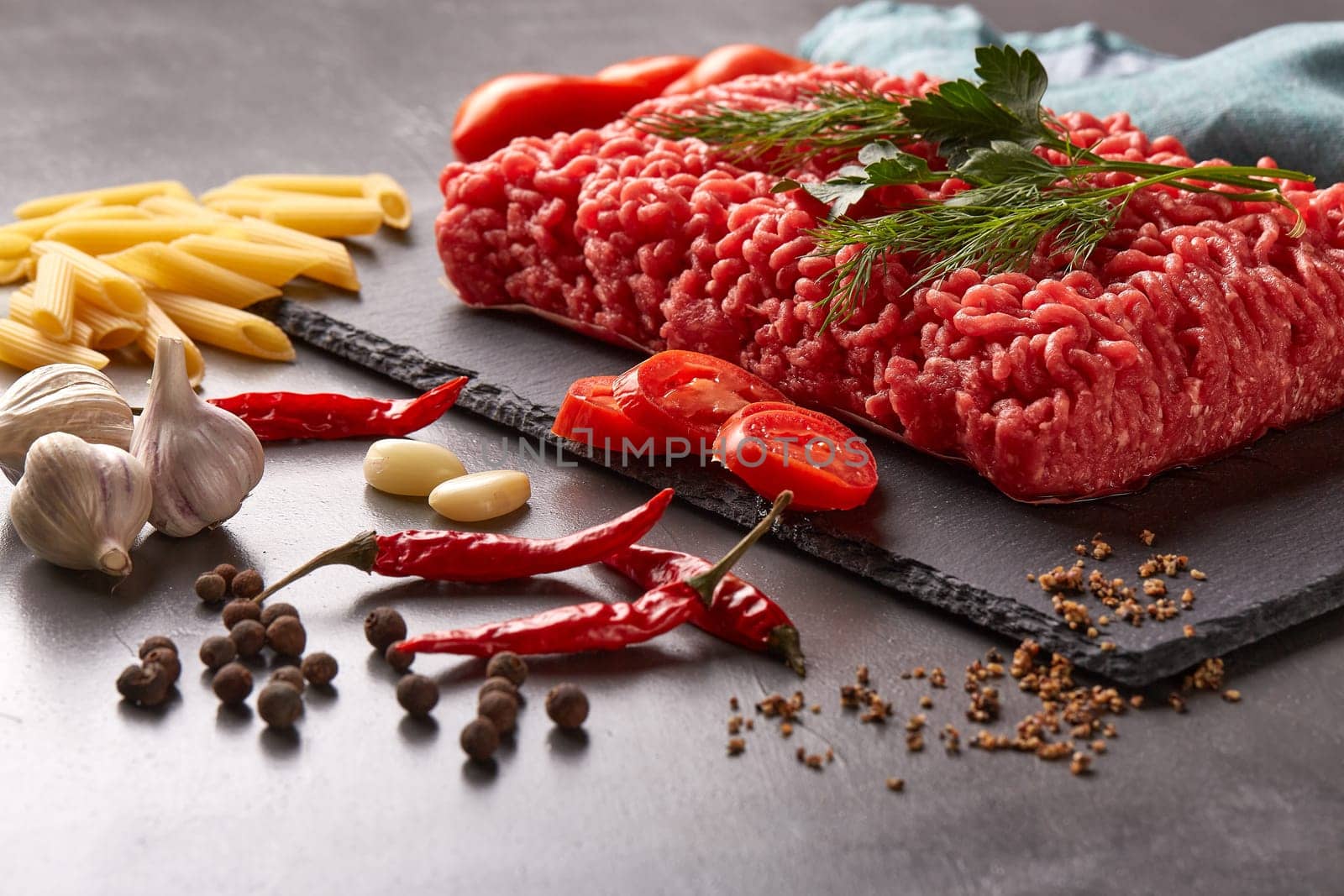Still life with fresh forcemeat from beef, vegetables, pasta and spices on a dark background.