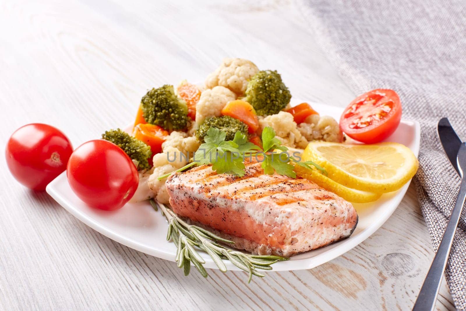 Grilled salmon fillet  garnished with vegetables, lemon, tomato, herbs lying on plate on wooden background. Healthy food. Keto diet.