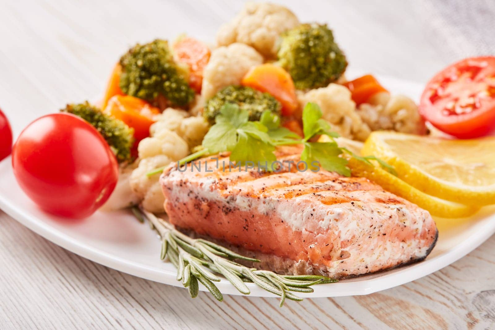 Grilled salmon fillet  garnished with vegetables, lemon, tomato, herbs lying on plate on wooden background. Healthy food. Keto diet.