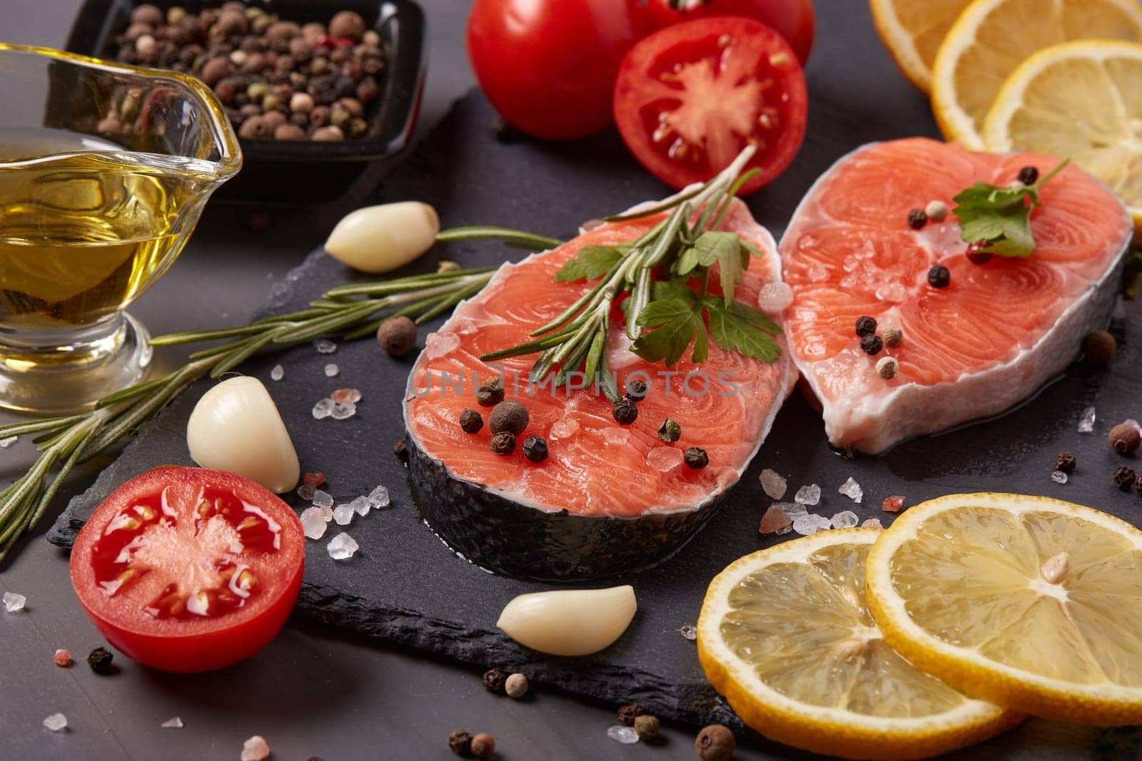 Fresh raw steak of salmon with spices and vegetables lying on stone cutting board on a black background.Top view.Seafood menu