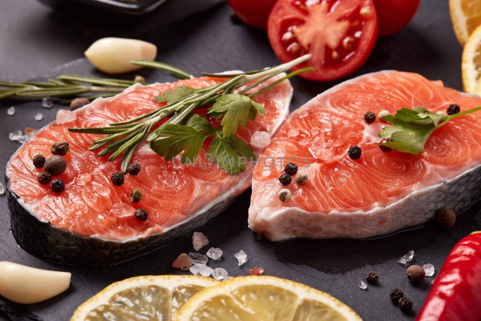 Fresh raw steak of salmon with spices and vegetables lying on stone cutting board on a black background. Seafood menu