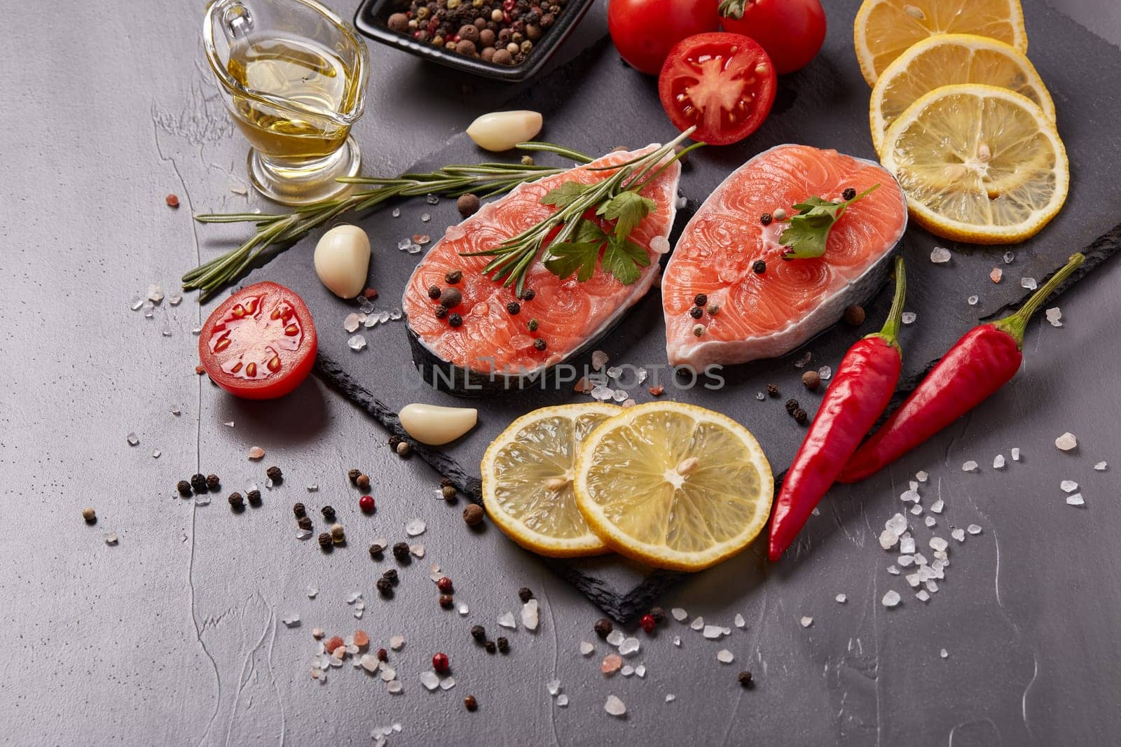 Fresh raw  steak of salmon with spices and vegetables lying on stone cutting board on a black background. Top view. Seafood menu