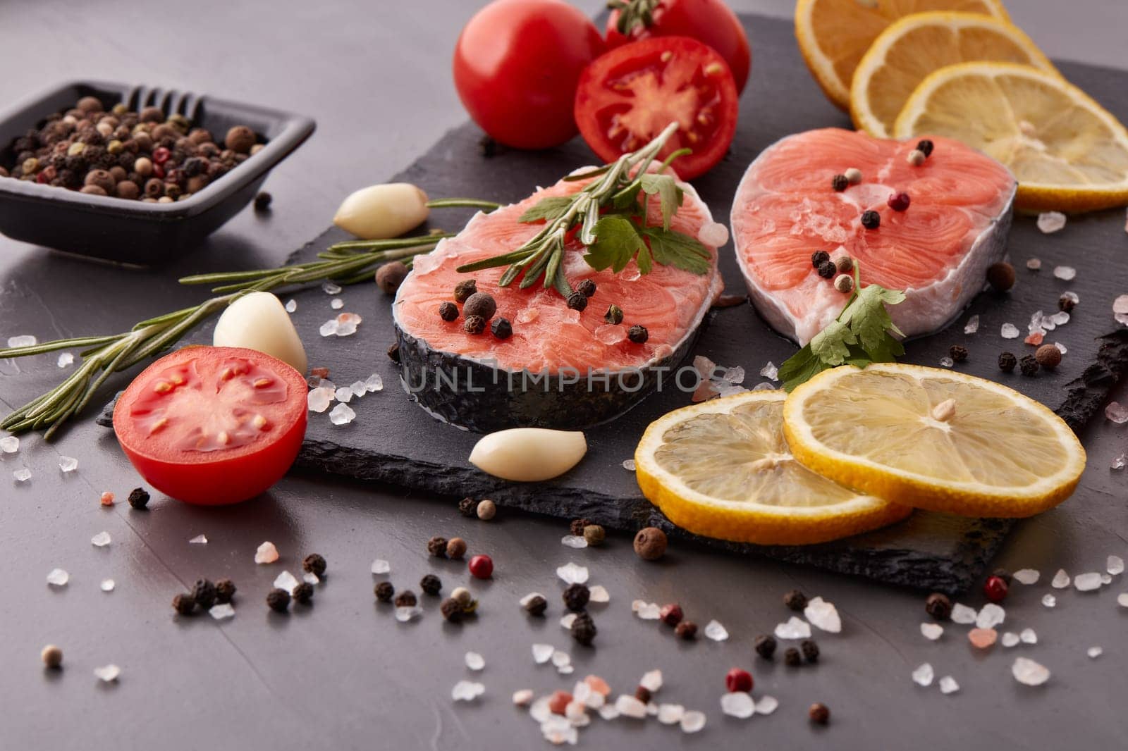 Fresh raw steak of salmon with spices and vegetables lying on stone cutting board on a black background. Seafood menu