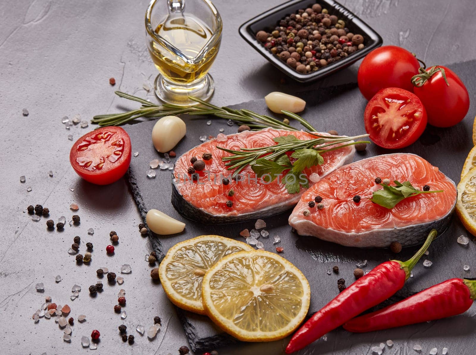 Fresh raw steak of salmon with spices and vegetables lying on stone cutting board on a black background.Top view.Seafood menu