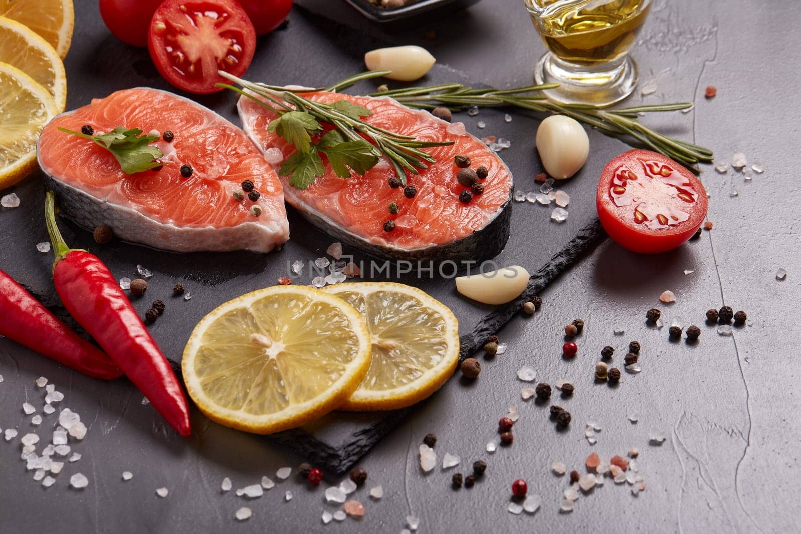 Fresh raw steak of salmon with spices and vegetables lying on stone cutting board on a black background. Seafood menu