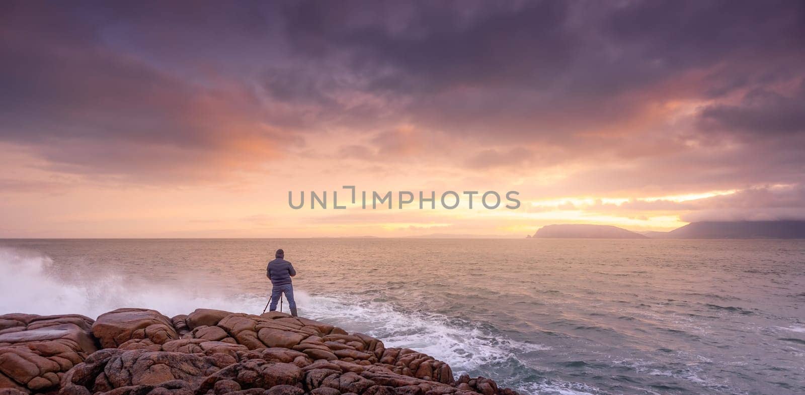 Photographer photographing waves crashing on rocks with amazing sunrise in background. Fanad Head peninsula at Wild Atlantic Way, Donegal, Ireland