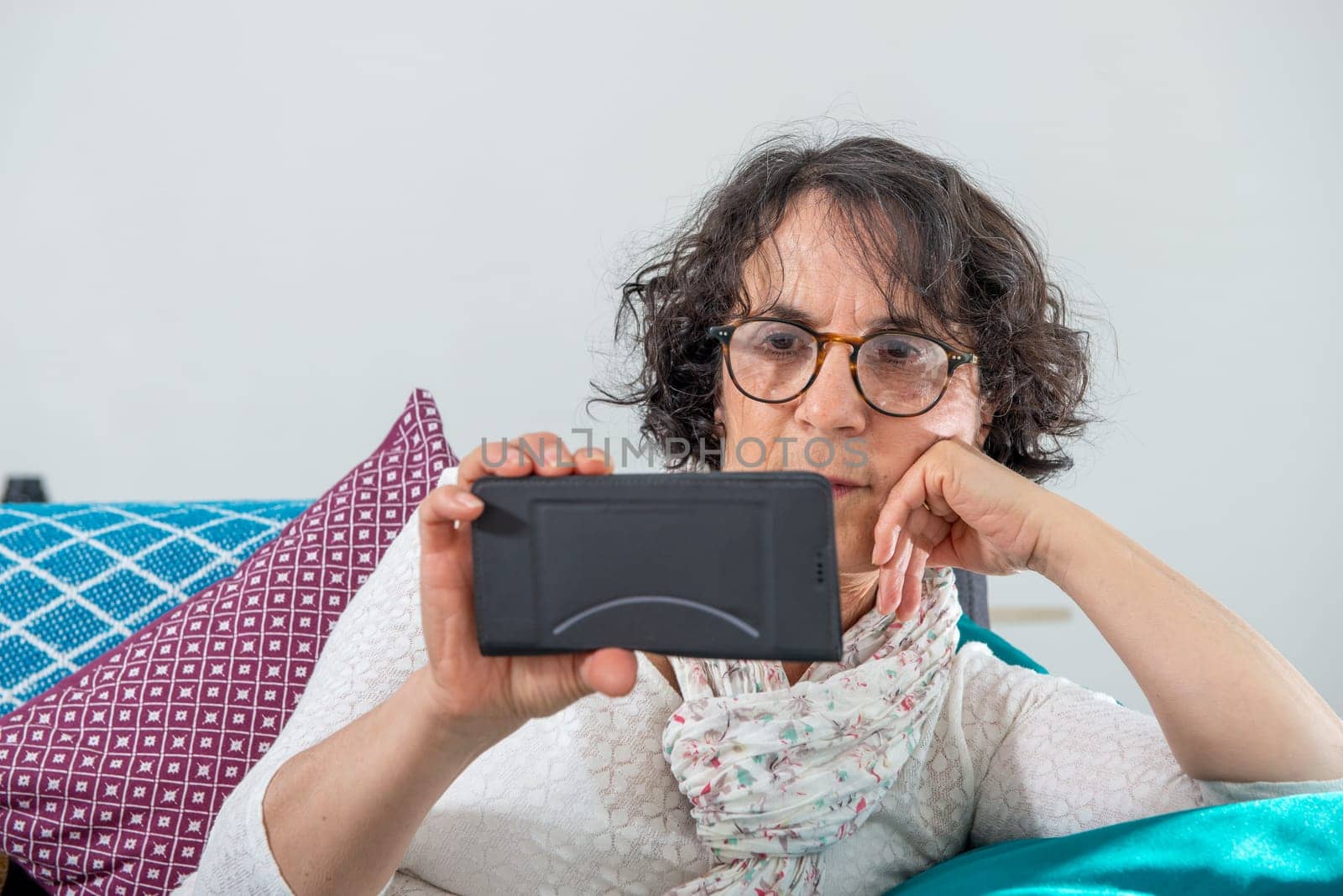 cheerful brunette senior woman using a smartphone while sitting on sofa