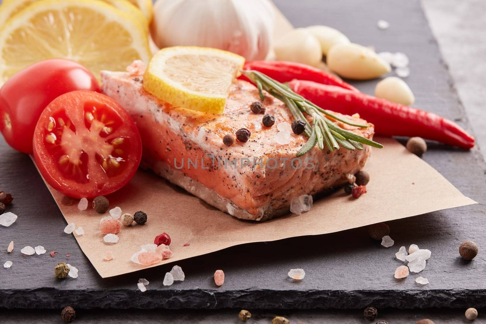 Grilled salmon fillet with spices and vegetables lying on stone cutting board on a grey background. Seafood menu.  Keto diet.