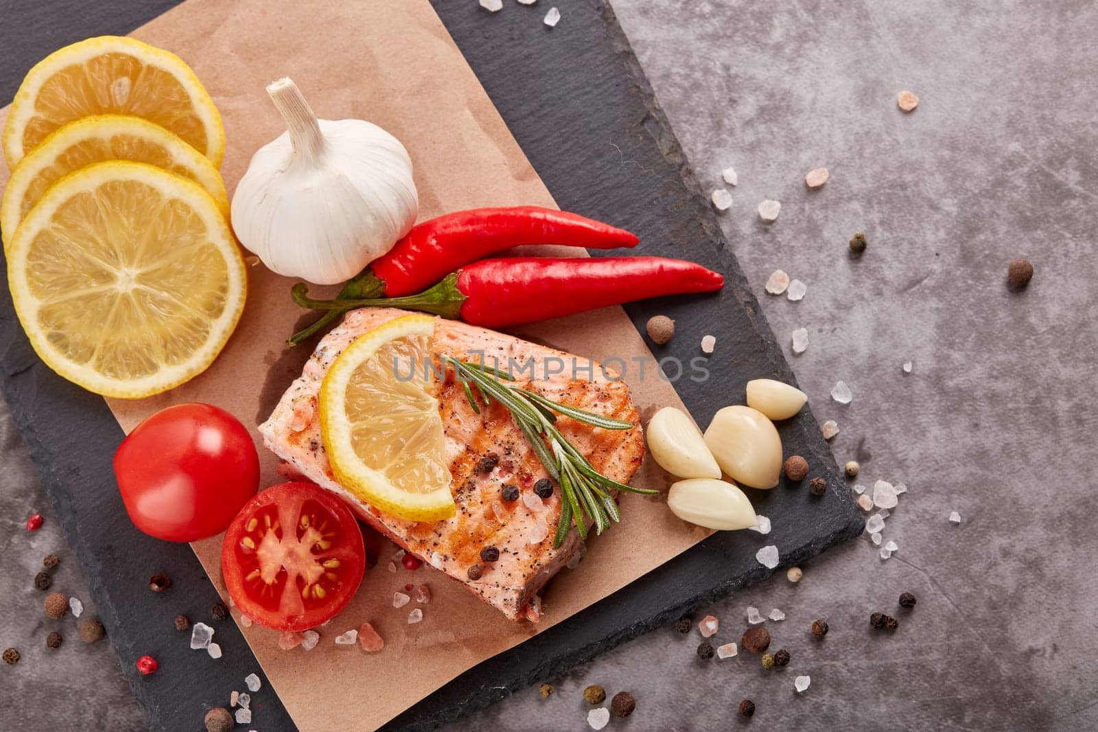 Grilled salmon fillet with spices and vegetables lying on stone cutting board on a grey background. Top view. Seafood menu.  Keto diet.