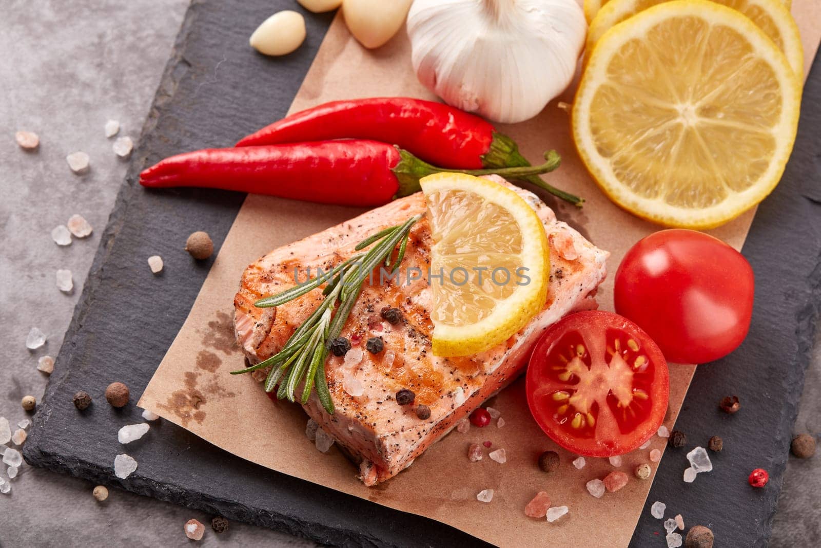 Grilled salmon fillet with spices and vegetables lying on stone cutting board on a grey background. Top view. Seafood menu.  Keto diet.