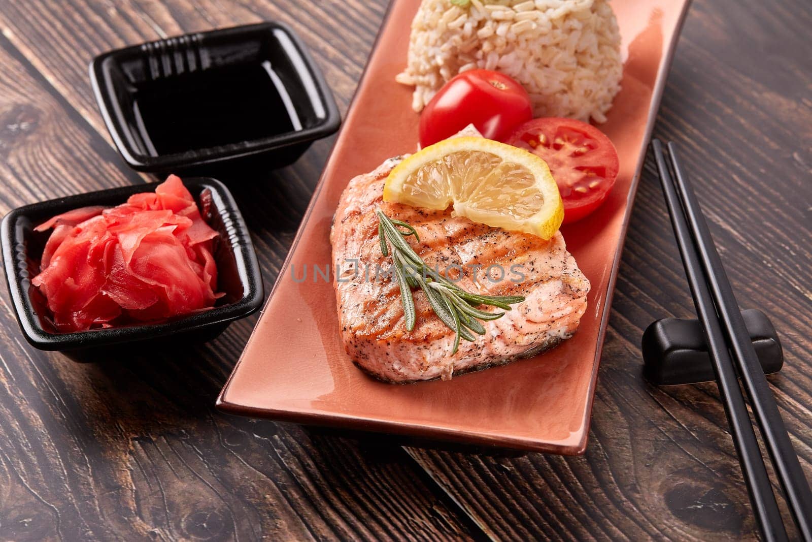 Grilled salmon fillet with rice, pickled ginger, soy sauce, tomato, lemon and herbs on dark wooden background. Top view. Healthy food.
