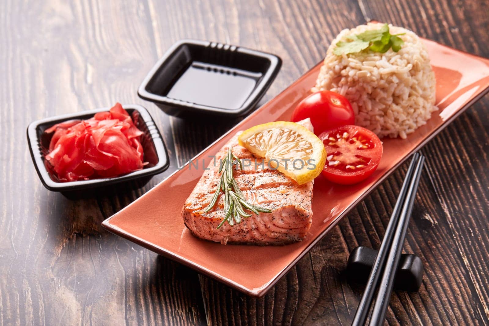Grilled salmon fillet with rice, pickled ginger, soy sauce, tomato, lemon and herbs on dark wooden background.  Healthy food.