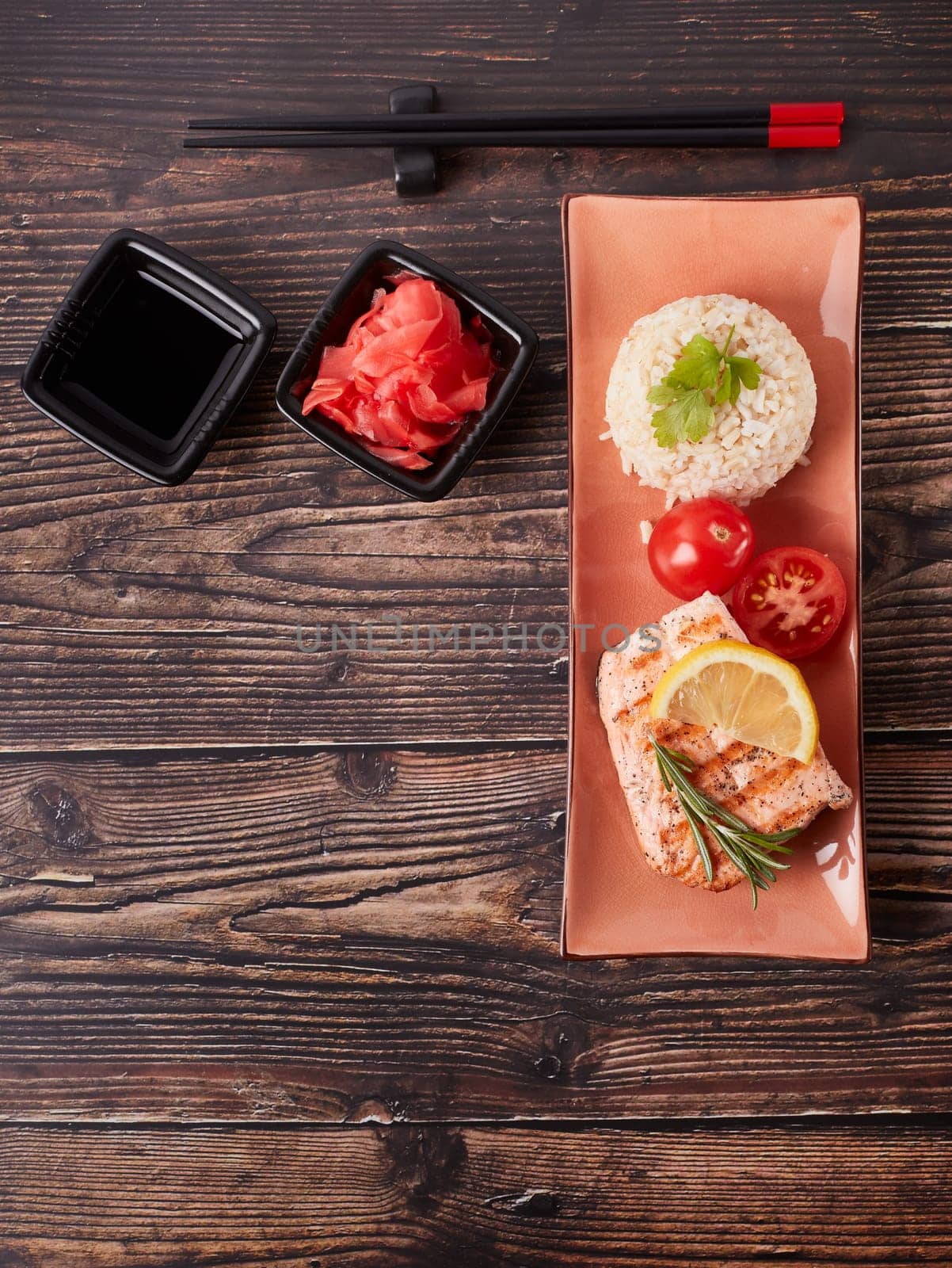 Grilled salmon fillet with rice, pickled ginger, soy sauce, tomato, lemon and herbs on dark wooden background. Top view with copy space. Healthy food.