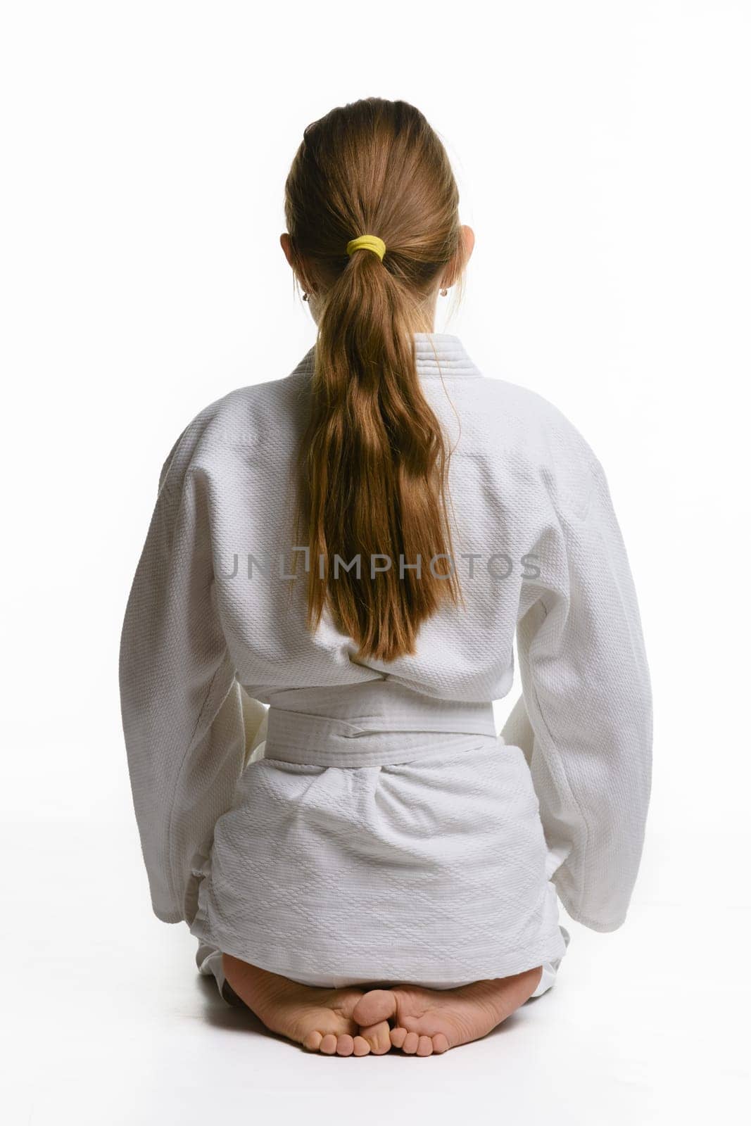 Girl in judo class, sitting on the floor, rear view