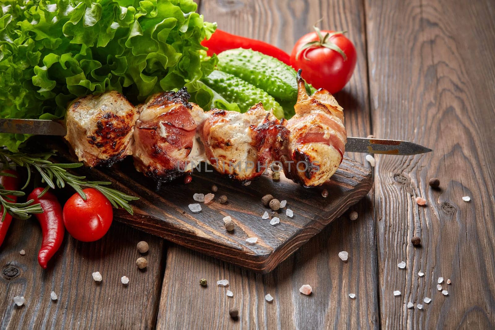 Shashlik from chicken with bacon. Grilled chicken (turkey) fillet on skewer and fresh vegetables with spices on stone cutting board on wooden background