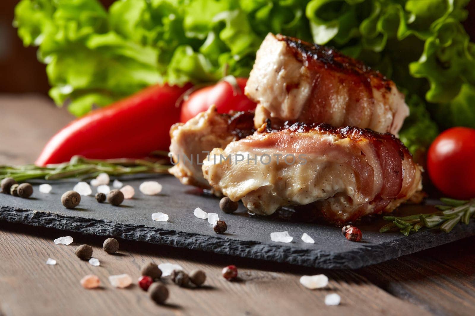 Bacon-wrapped grilled chicken (turkey)  fillet with fresh vegetables and spices on stone cutting board on wooden background