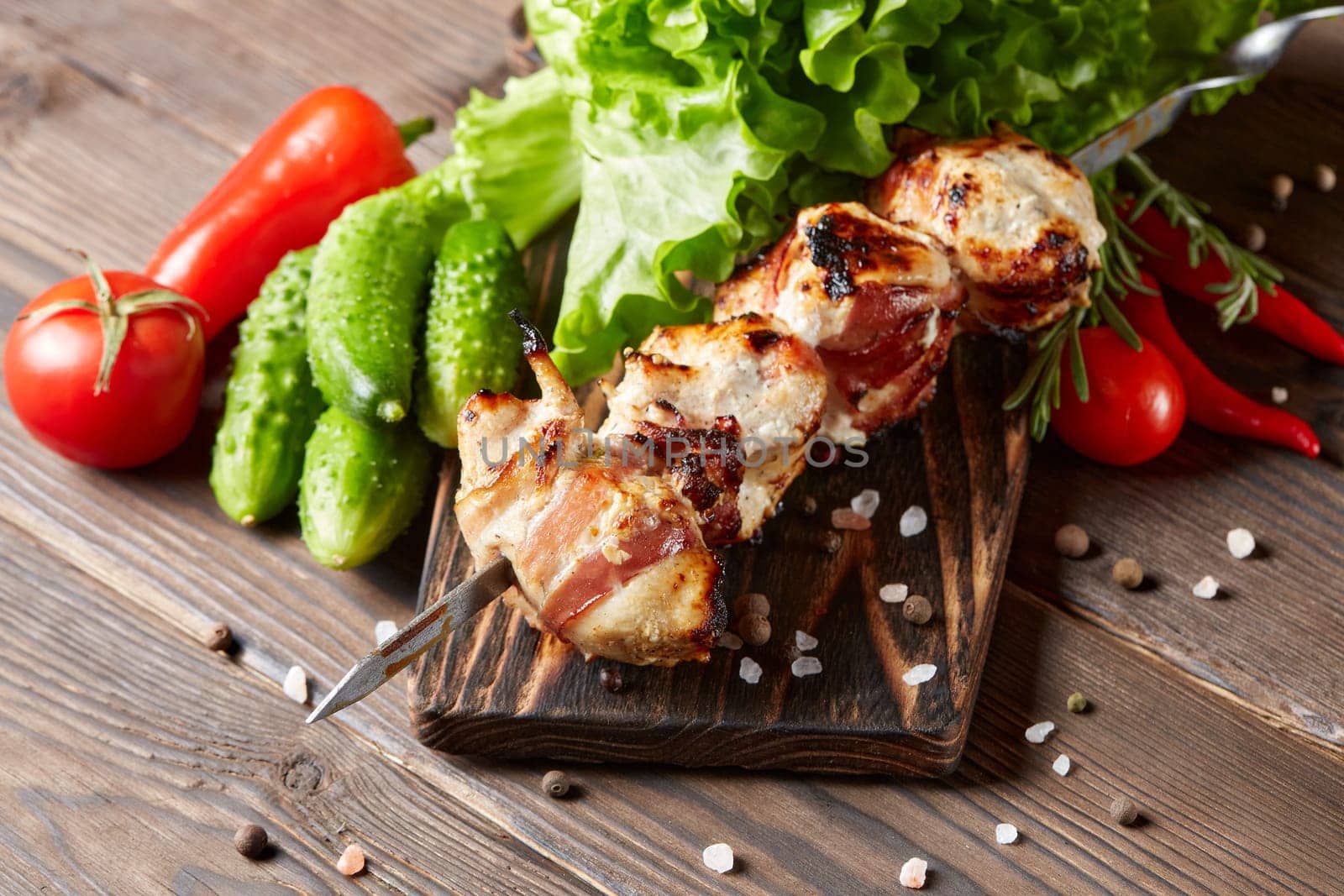 Shashlik from chicken with bacon. Grilled chicken (turkey) fillet on skewer and fresh vegetables with spices on stone cutting board on wooden background