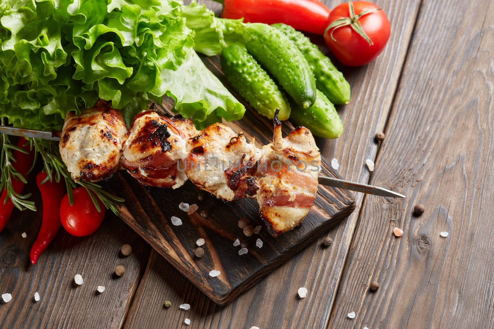 Shashlik from chicken with bacon. Grilled chicken (turkey) fillet on skewer and fresh vegetables with spices on stone cutting board on wooden background