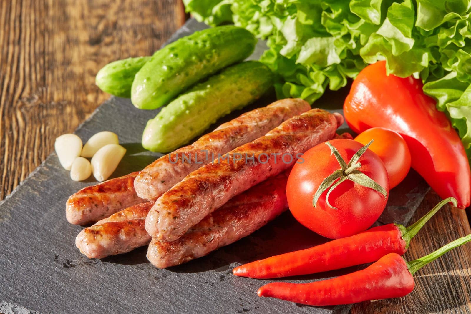 Grilled pork sausages  with fresh vegetables  on stone cutting board on wooden background.