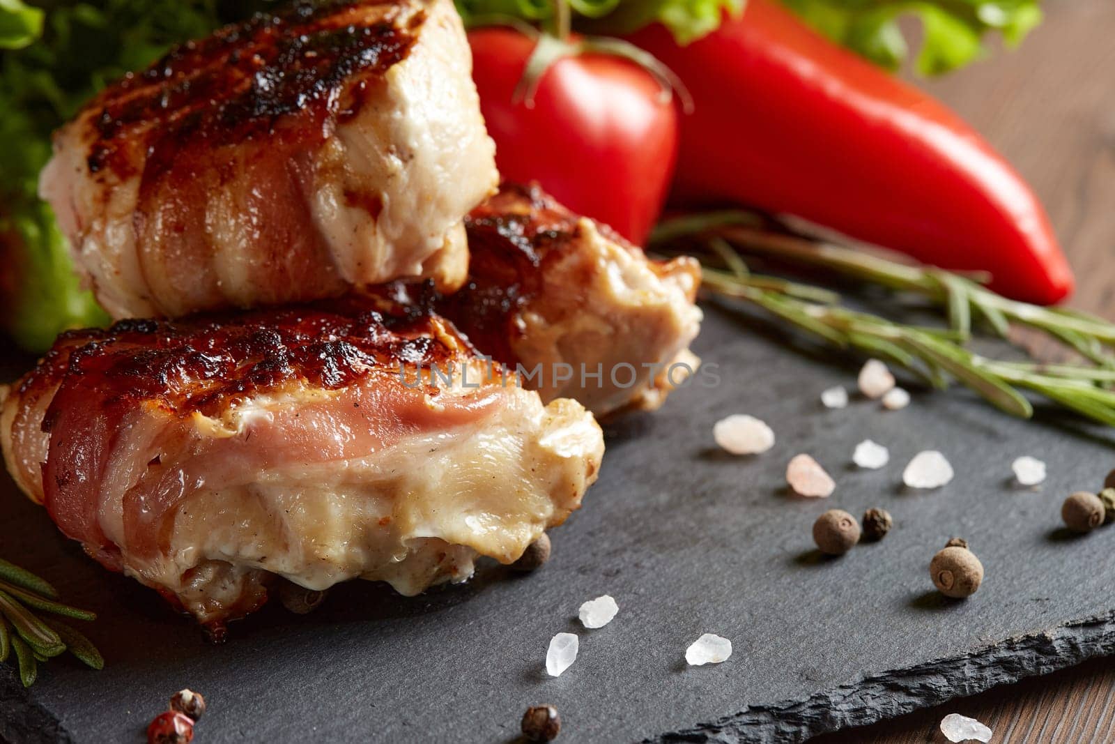 Bacon-wrapped grilled chicken (turkey)  fillet with fresh vegetables and spices on stone cutting board on wooden background