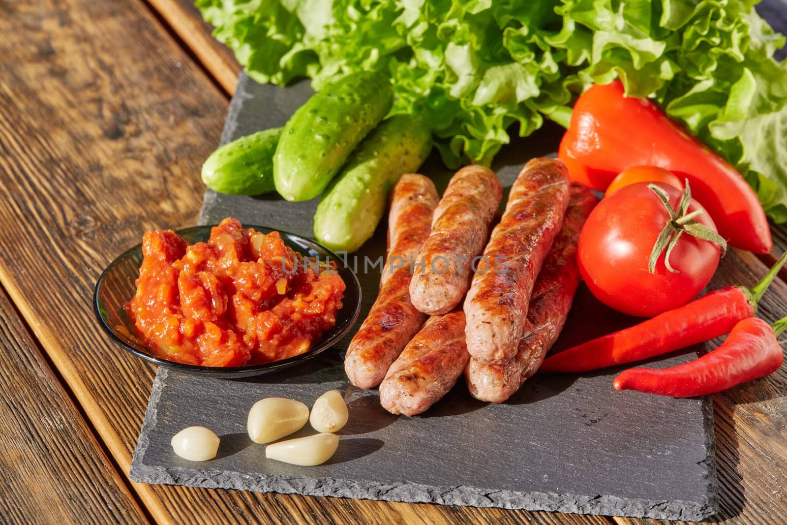 Grilled pork sausages  with fresh vegetables  on stone cutting board on wooden background.