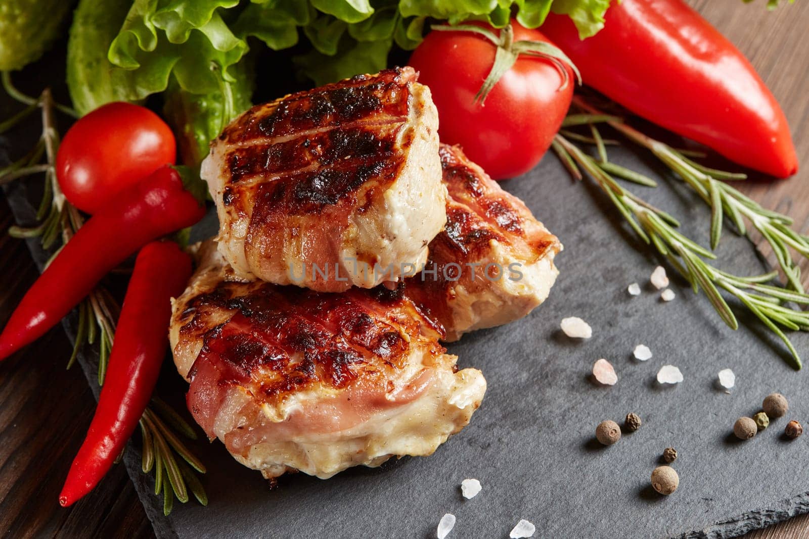 Bacon-wrapped grilled chicken (turkey)  fillet with fresh vegetables and spices on black stone cutting board on