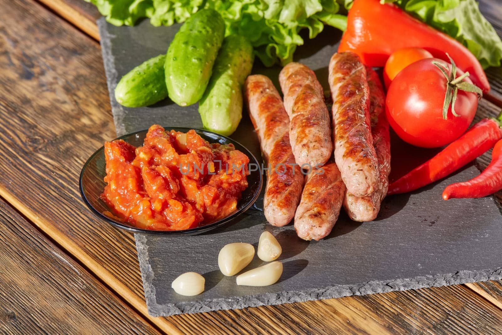 Grilled pork sausages  with fresh vegetables  on stone cutting board on wooden background.
