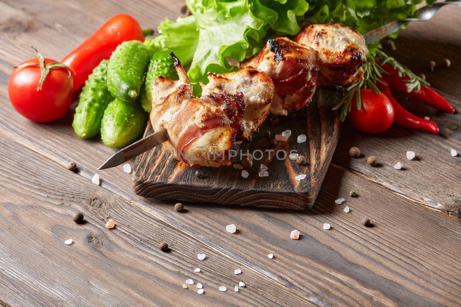Shashlik from chicken with bacon. Grilled chicken (turkey) fillet on skewer and fresh vegetables with spices on stone cutting board on wooden background