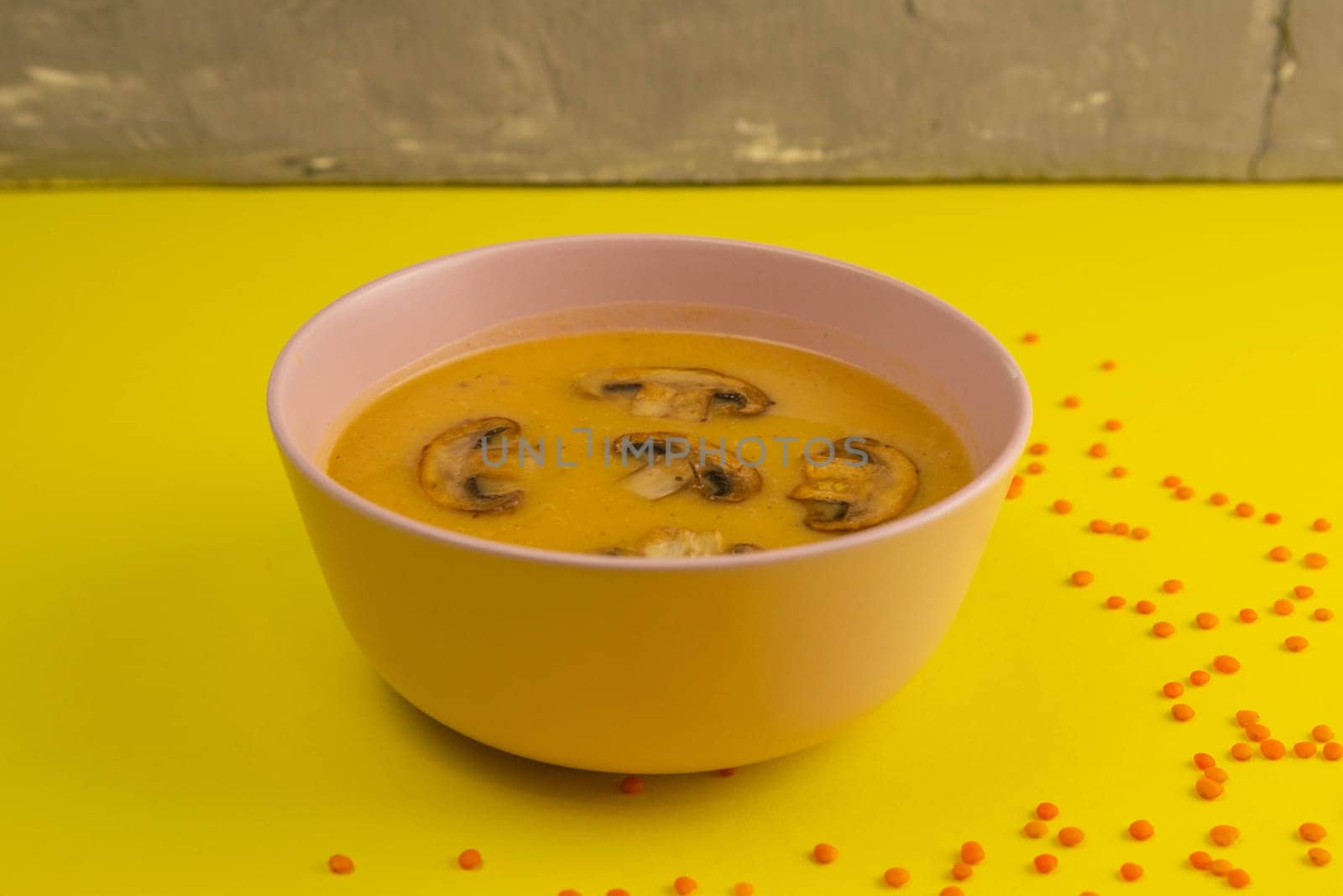 Pea soup with croutons and mushroom on a colored towel that stands on a yellow table.