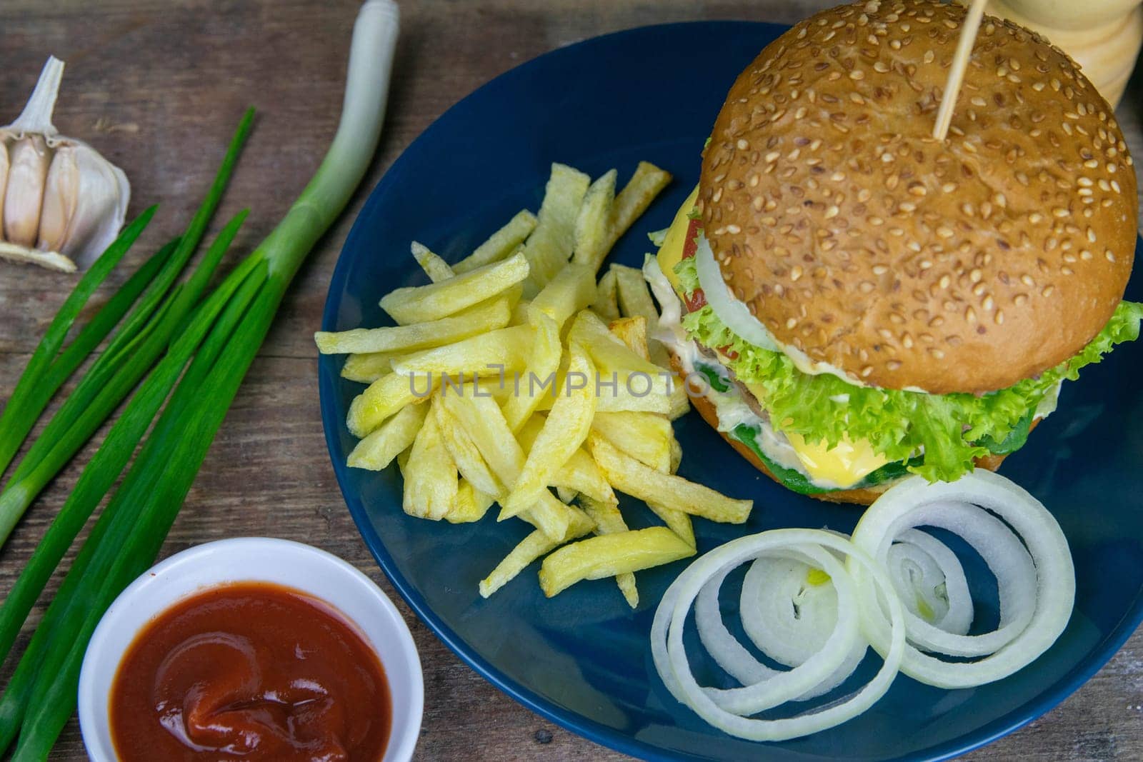 Two hamburgers close-up on a round wooden board, next to, tomatoes, chopped onions and spinach leaves. Top views with clear space