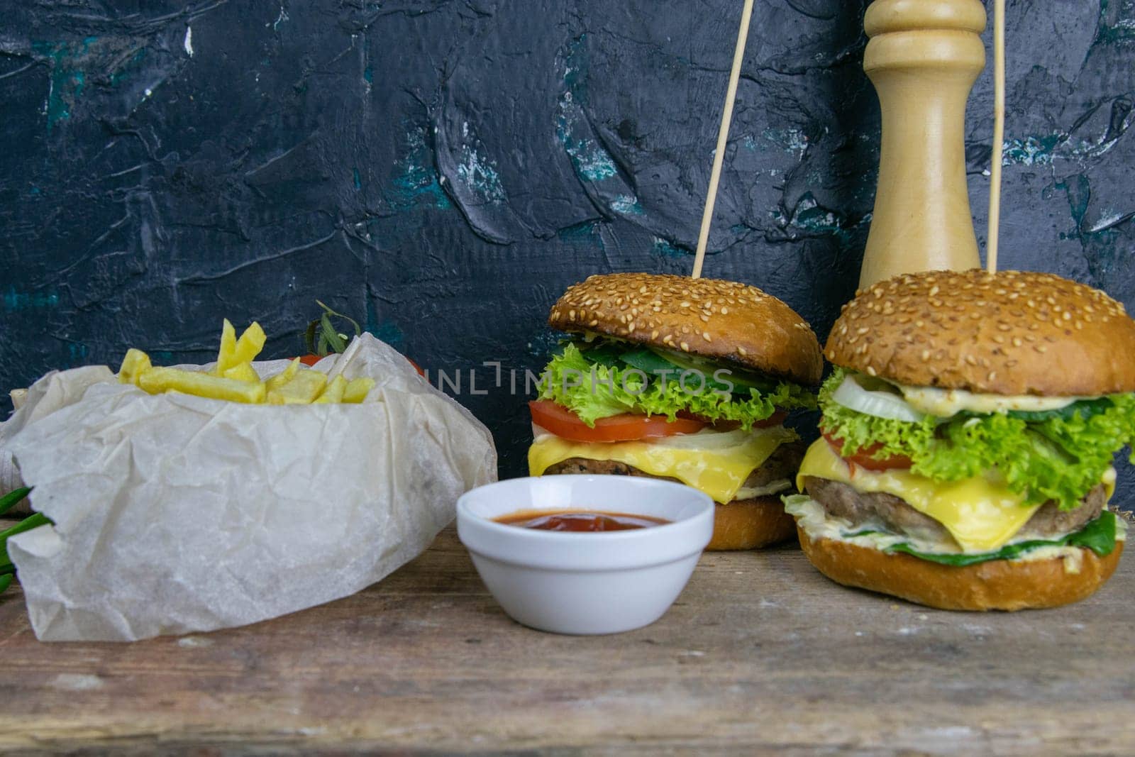 Two hamburgers close-up on a round wooden board, next to, tomatoes, chopped onions and spinach leaves.