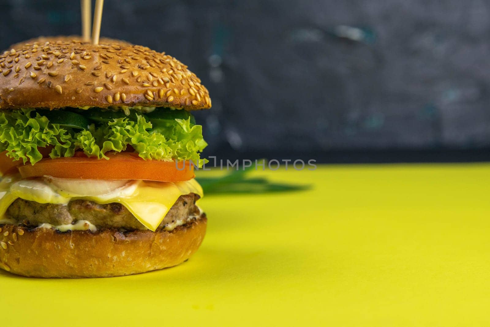 Two hamburgers close-up on a round wooden board, next to, tomatoes, chopped onions and spinach leaves.