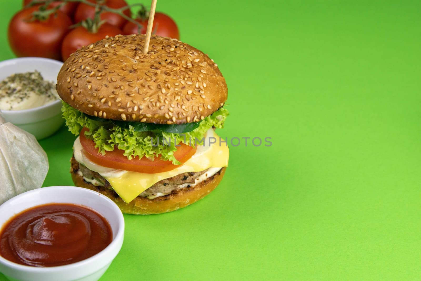 Two hamburgers close-up on a round wooden board, next to, tomatoes, chopped onions and spinach leaves.