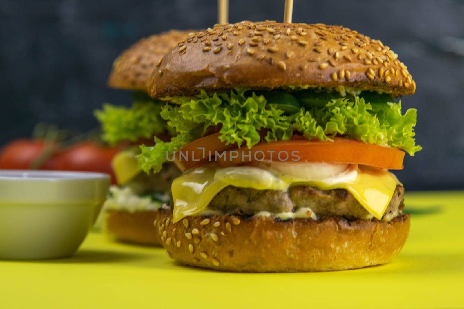 Two hamburgers close-up on a round wooden board, next to, tomatoes, chopped onions and spinach leaves.