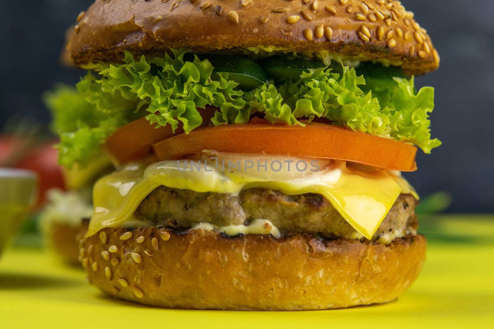 Two hamburgers close-up on a round wooden board, next to, tomatoes, chopped onions and spinach leaves.