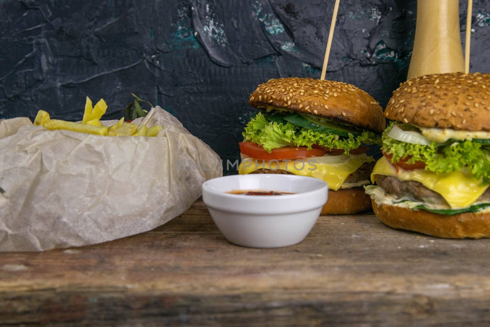 Two hamburgers close-up on a round wooden board, next to, tomatoes, chopped onions and spinach leaves.