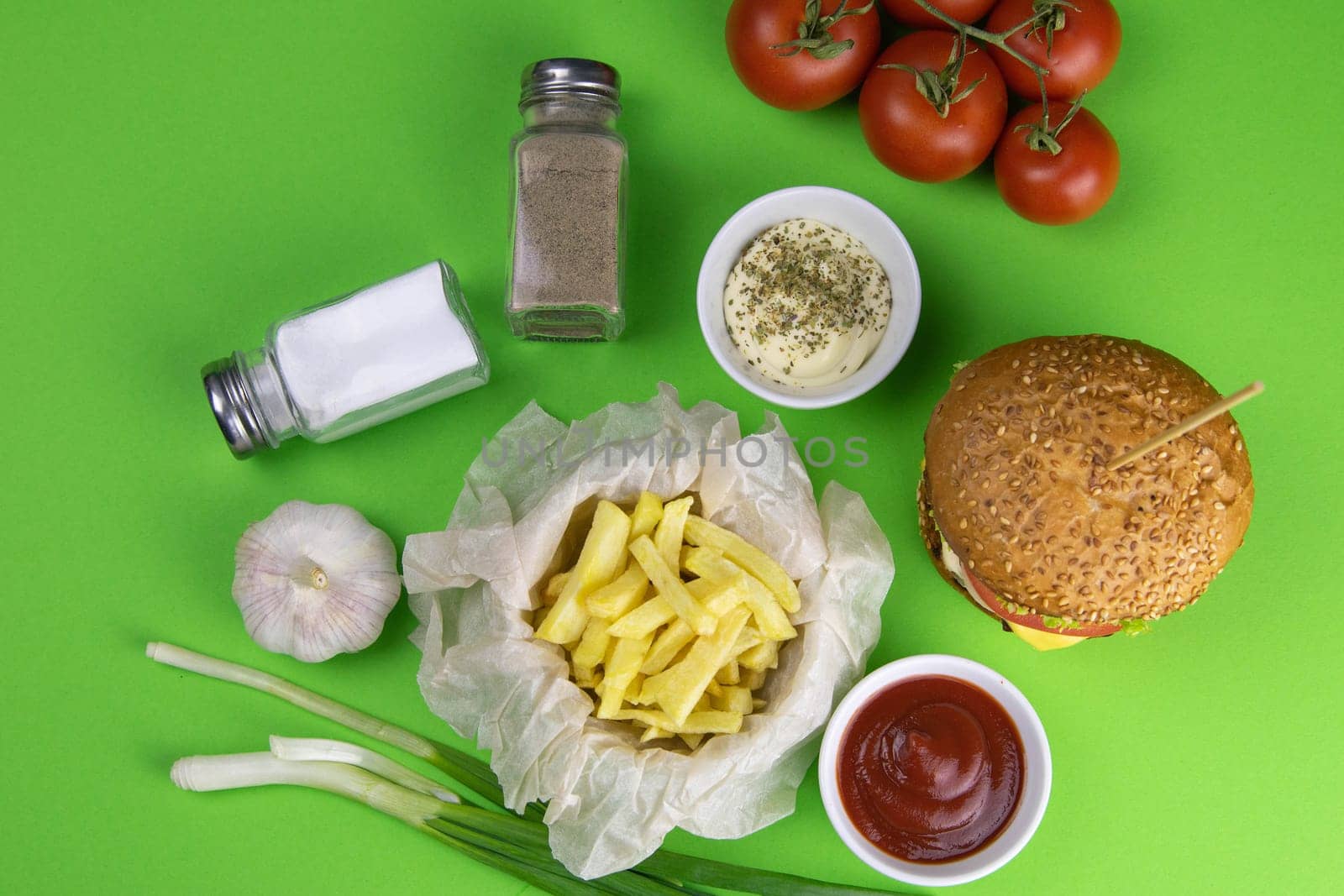 Two hamburgers close-up on a round wooden board, next to, tomatoes, chopped onions and spinach leaves.