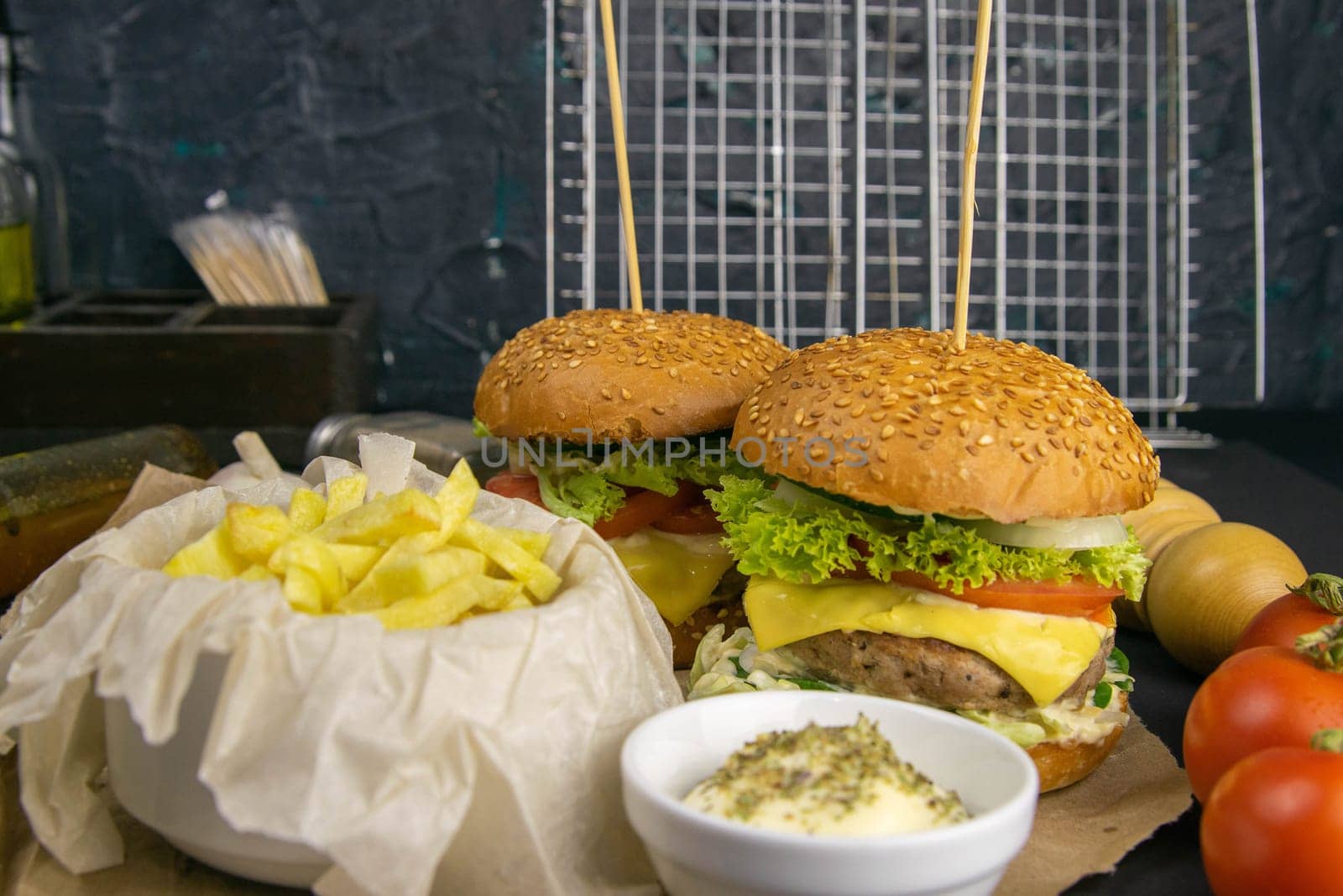 Two hamburgers close-up on a round wooden board, next to, tomatoes, chopped onions and spinach leaves.