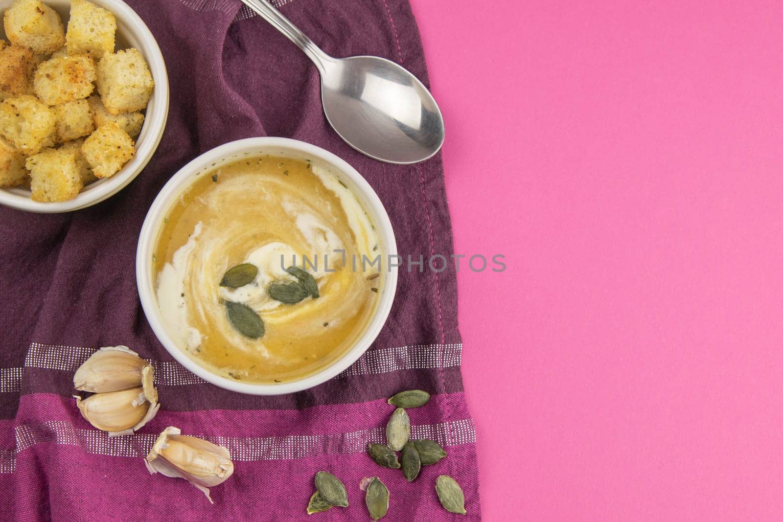 Pea soup with croutons stands on a green towel, next to there are tomatoes, toasts of pumpkin seeds, everything stands on the yellow table.